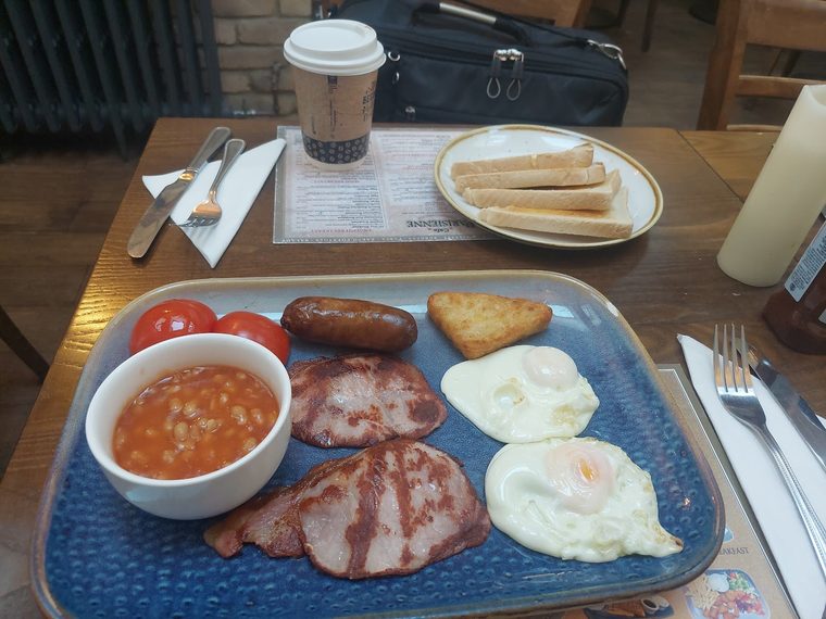 Breakfast plate of back bacon, sausage, two fried eggs, hash brown, tomato and beans.