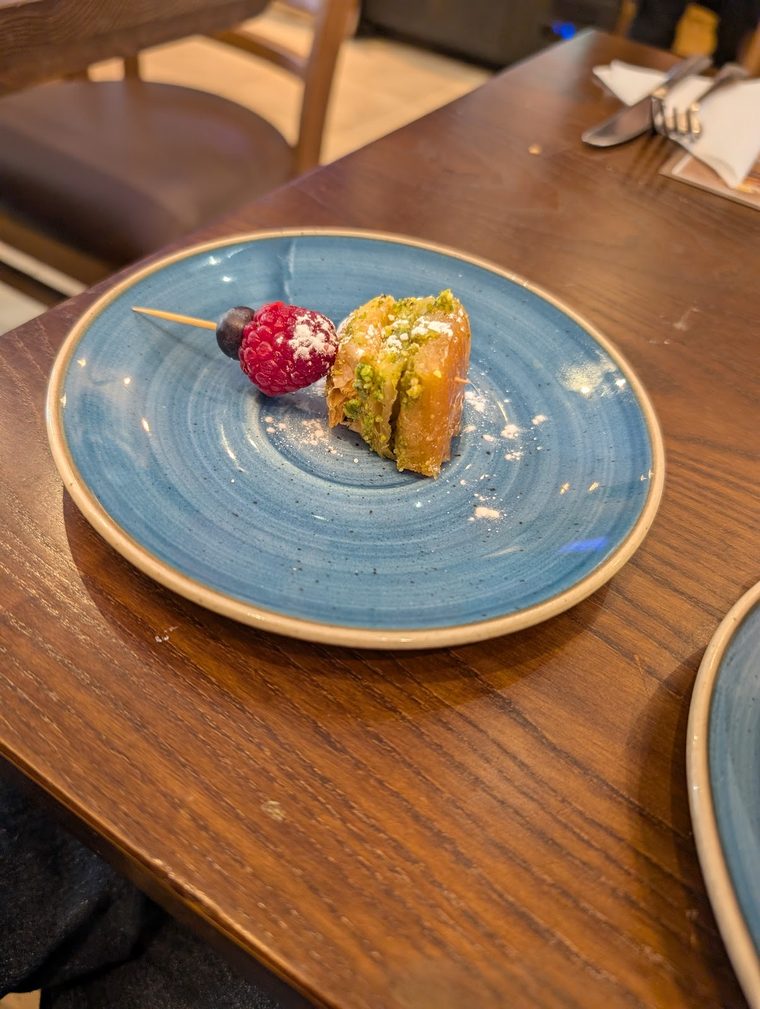 A slice of pistachio baklava with a berry garnish on a rustic blue plate.